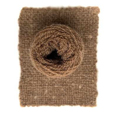 A ball of Castlemilk Moorit sheep wool presented on a piece of handwoven fabric made from the same yarn.