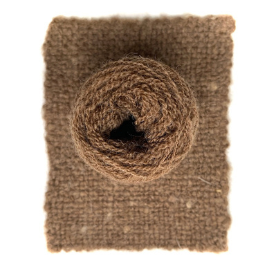 A ball of Castlemilk Moorit sheep wool presented on a piece of handwoven fabric made from the same yarn.