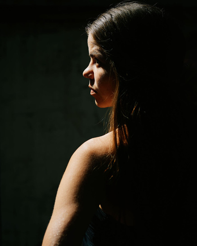 Silhouette af kvinde hvor lyset rammer hendes ene arm og side af ansigtet.