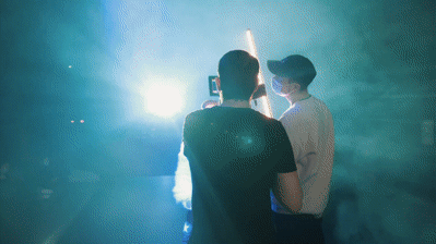 To mænd står bag et kamera og filmer med neonlys.