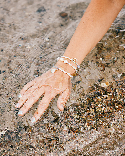 Hånd med armbånd på rører ved vand ved stranden