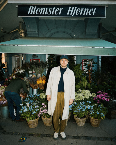 Mand står i hvid frakke med kasket foran en blomsterbutik