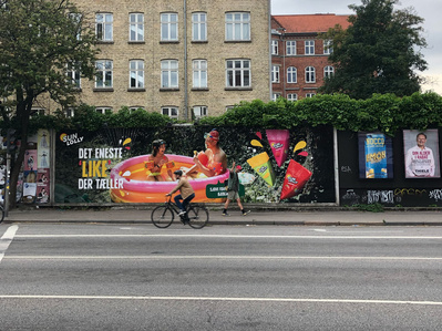 Vej med reklame i baggrunden for sun lolly og mennesker der går og cykler forbi