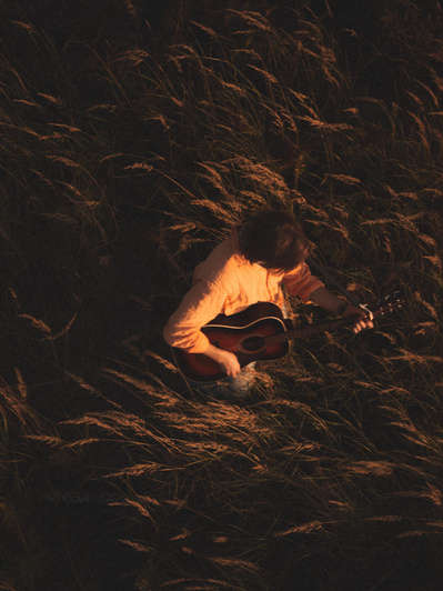 Mand står på en mark i en orange skjorte og spille på sin guitar