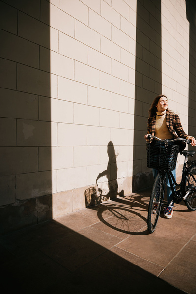 Kvinde går med cykel ved flot hvid bygning og sollys i ansigtet