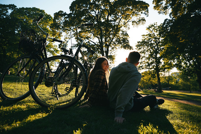 Mand og kvinde sidder og hygger på picnic i solnedgangen med deres cykler ved siden af på græsset