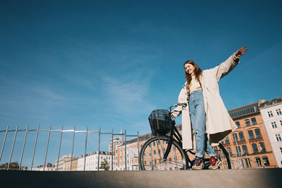 Kvinde i frakke går og balancerer på kant med cykel og blå himmel 