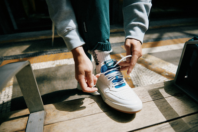 Person binder snørebånd på hvide sneakers I flot sollys 