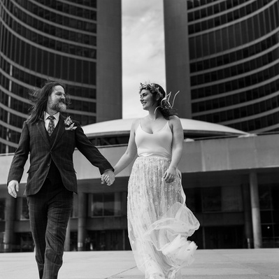 A couple walking away from Toronto City Hall, dressed in their wedding clothing