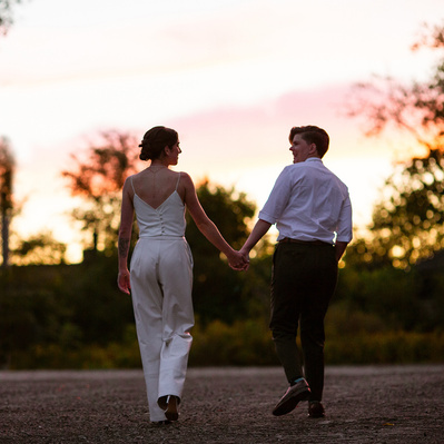 A newly married couple walk toward a sunset backdrop 