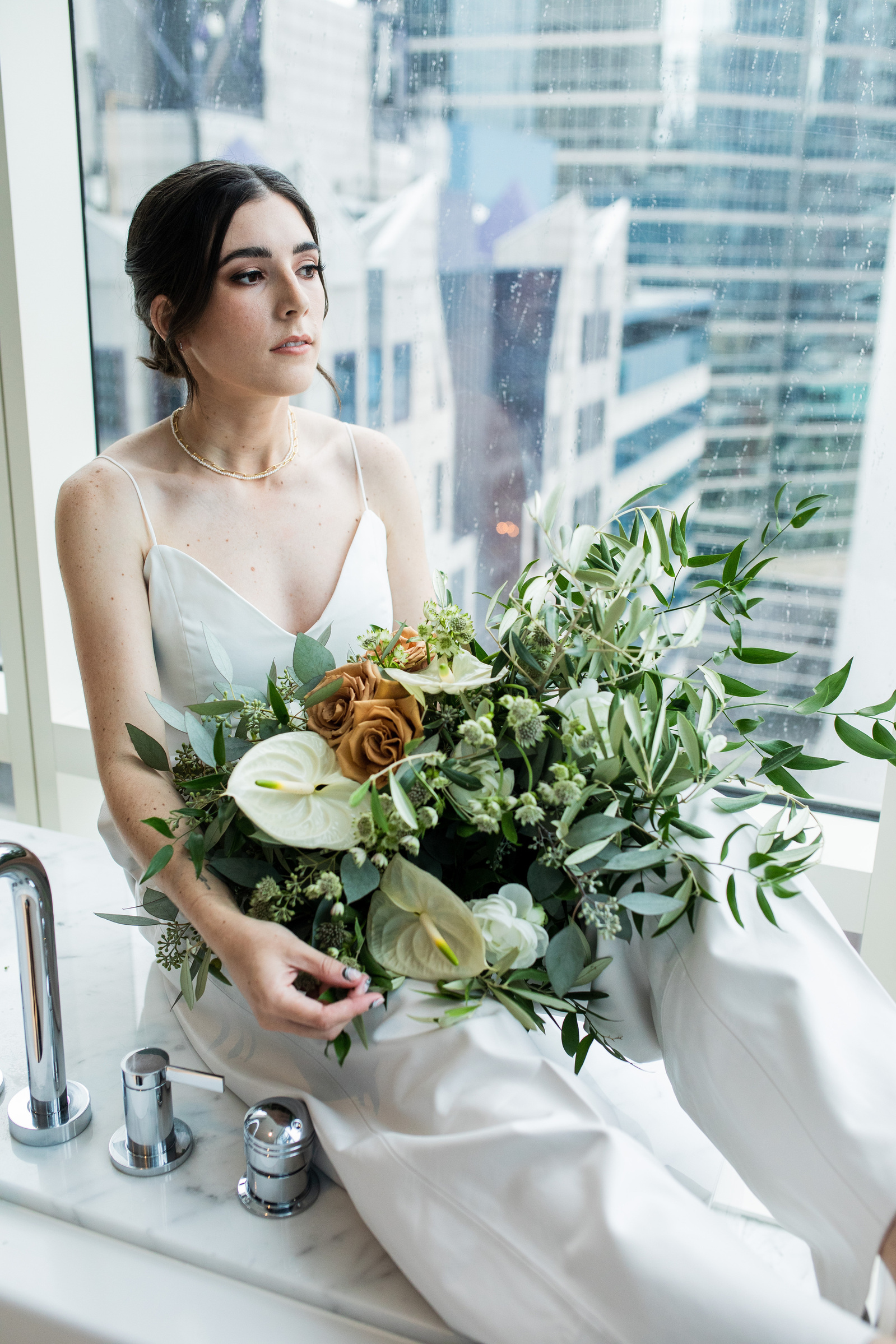 A bride in a white jumpsuit, holding her bouquet in a bathtub