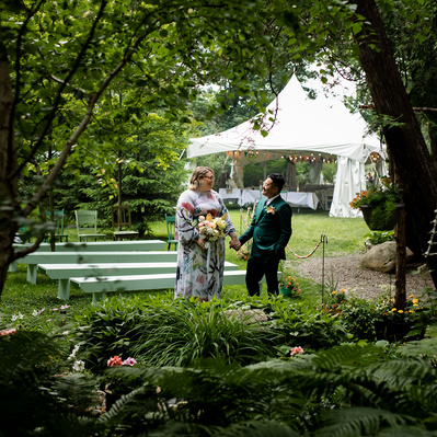 A couple facing each other, dressed for their wedding, in a grassy area