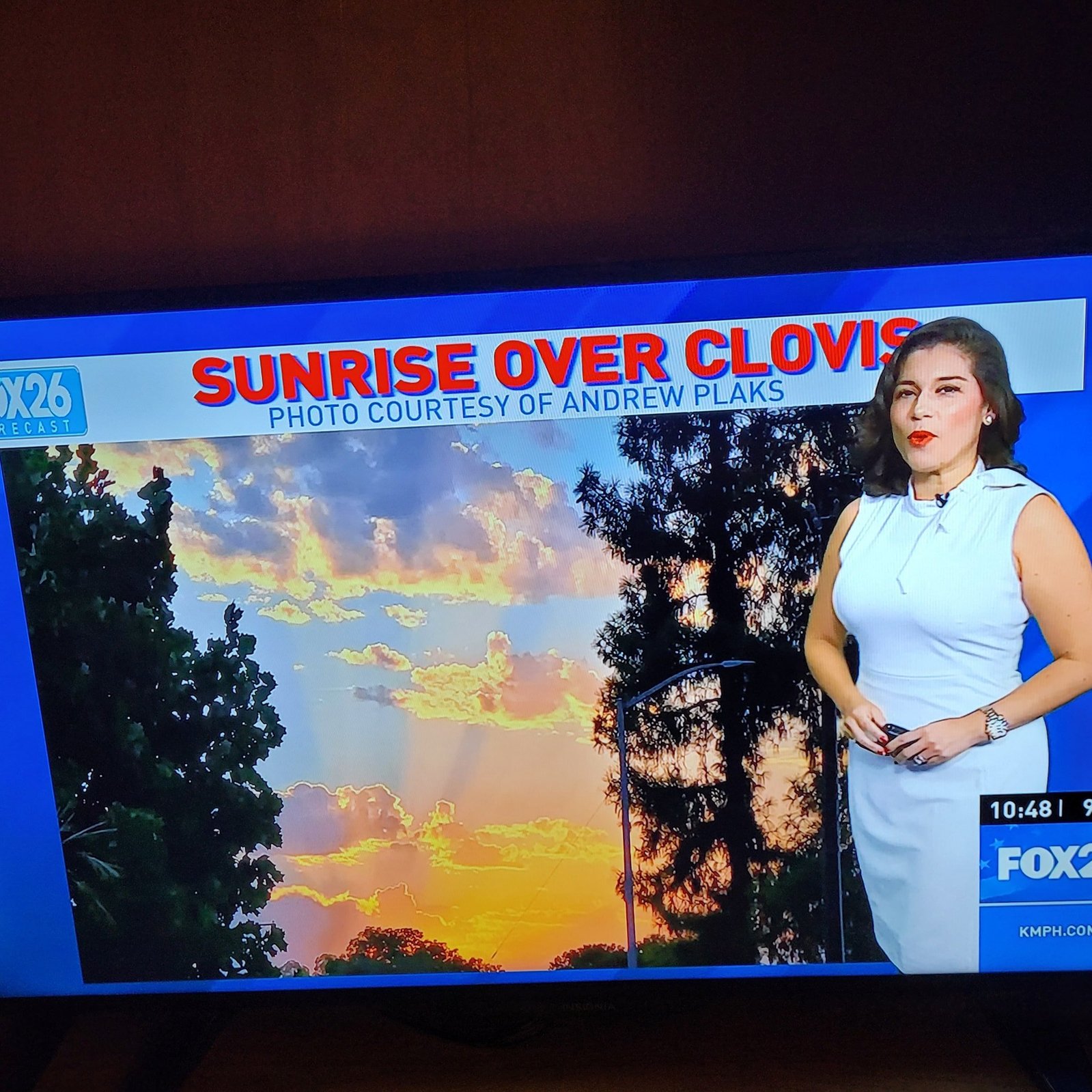 Newscaster gesturing over photo of sunrise. Text above reads: Sunrise Over Clovis Photo Courtesy of Andrew Plaks