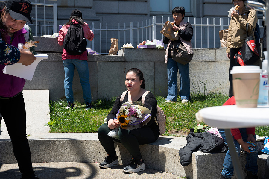 A woman sits with a bouquet of flowers in front of San Francisco's City Hall building on May 11, 2023. Families gathered to speak to city council members about lack of resources the city offers to houseless families. (Karina Patel/SF City Vitals)