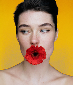Anja Winkelmann photographed in Paris by Adam Amouri. she is looking away, she has a red flower on her mouth with a yellow background. Bare shoulders
