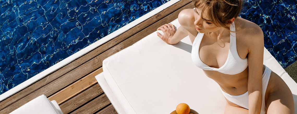 woman relaxing on a sun-bed on the edge of a swimming pool