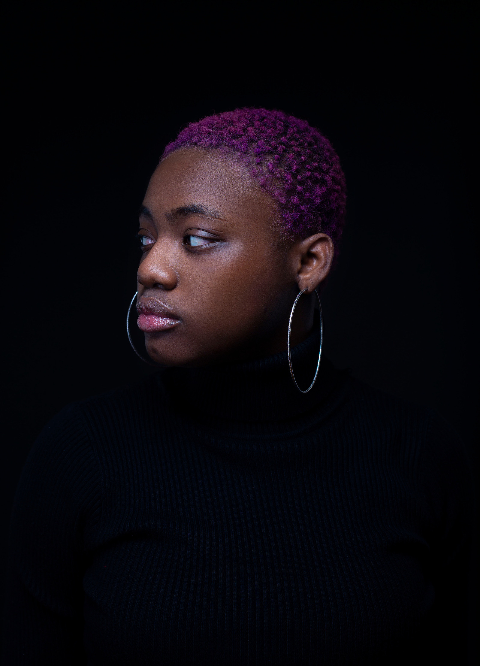 Woman with very short purple hair stares to her right