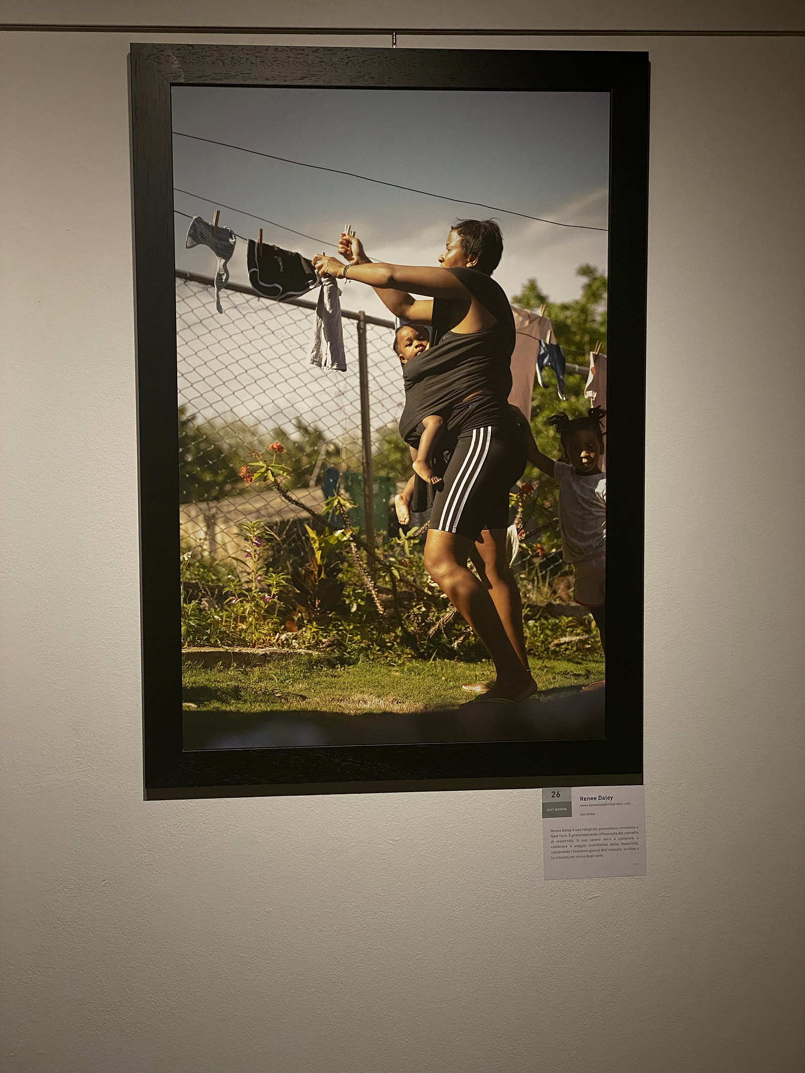 A picture of a fine art portrait of a woman hanging out clothes while her baby is strapped to her body