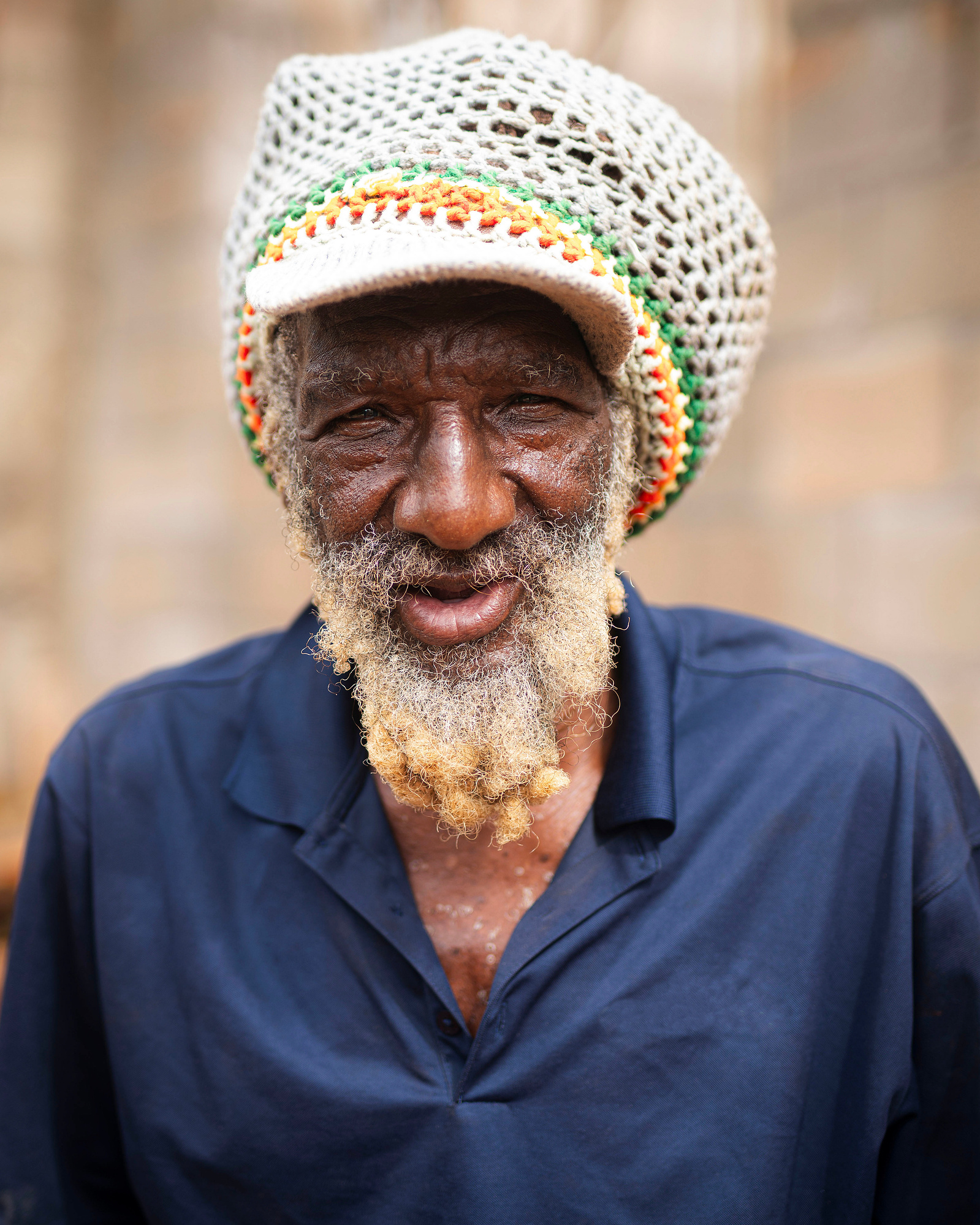 A rastafarian man wearing blue shirt with a knitted hat. 