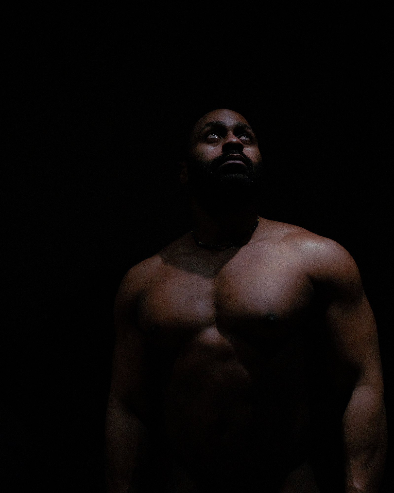 Black man in dark room looks up at light
