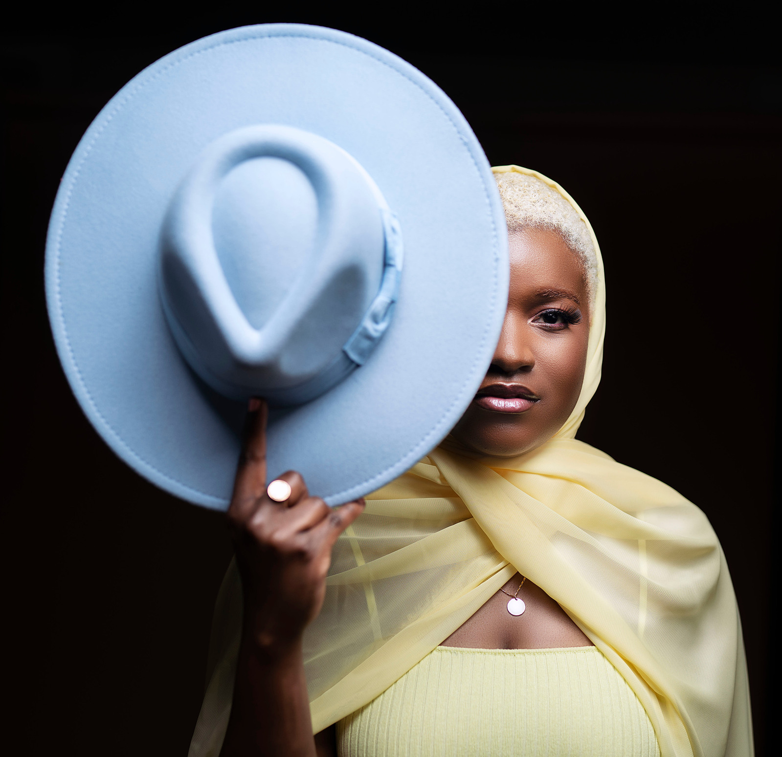 woman wearing a hijab holding a blue fedora  hat