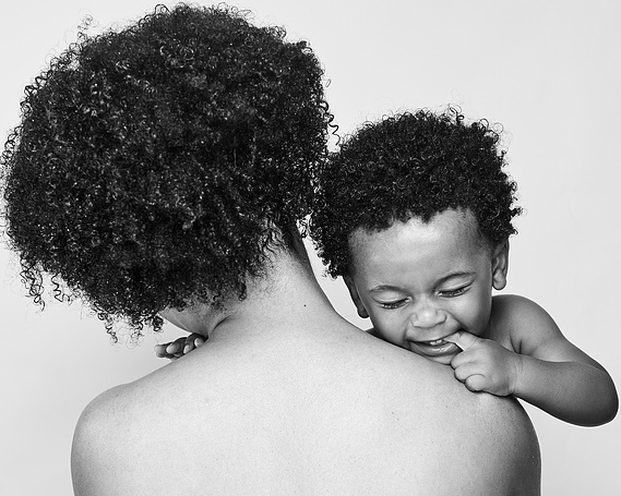 Portrait of mother with curly hair holding her baby son while the son laughs and her back turned to the camera.