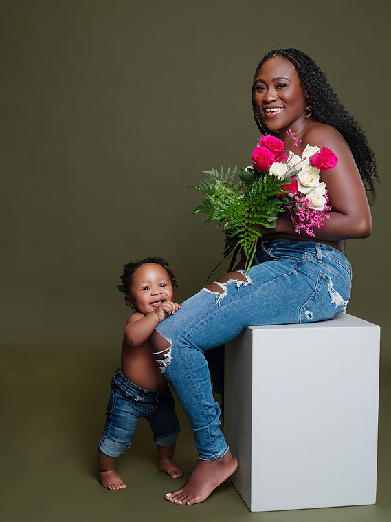 black mother holding a bunch of flowers while her baby stands next to her