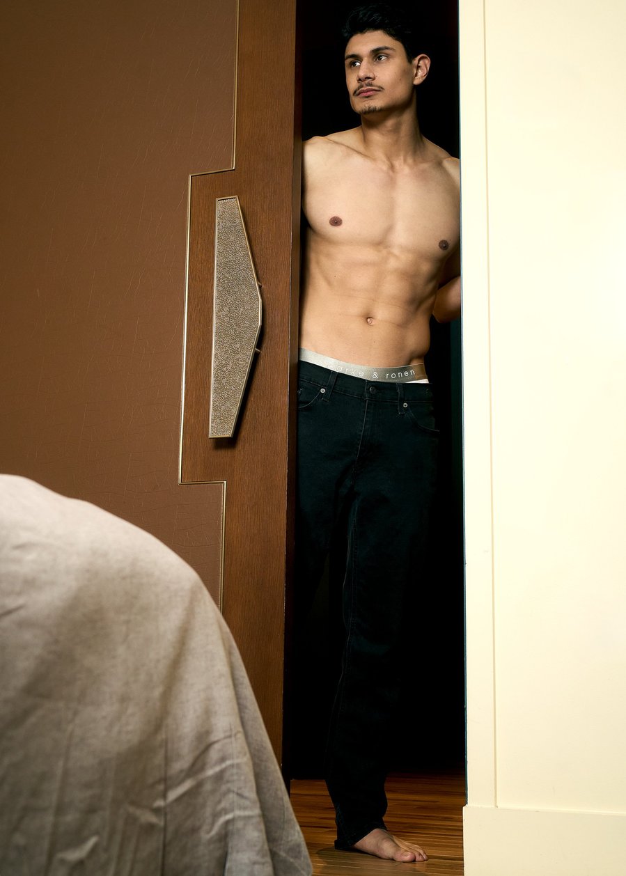 A male model wearing Parke & Ronen underwear and standing in a doorway in a hotel room