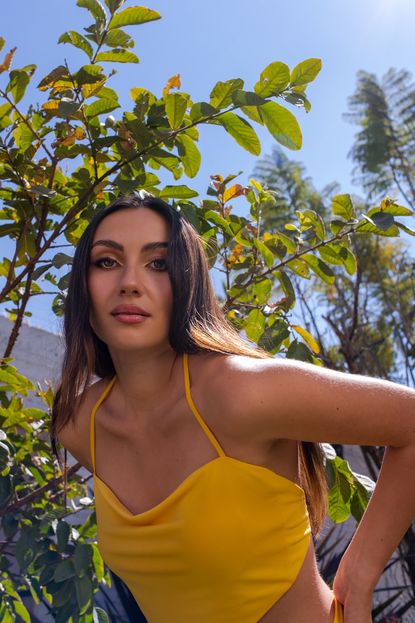retrato editorial en exterior con modelo en vestido entallado amarillo, maquillaje profesional, a la sombra del árbol, inclinada hacia la cámara, puebla, méxico