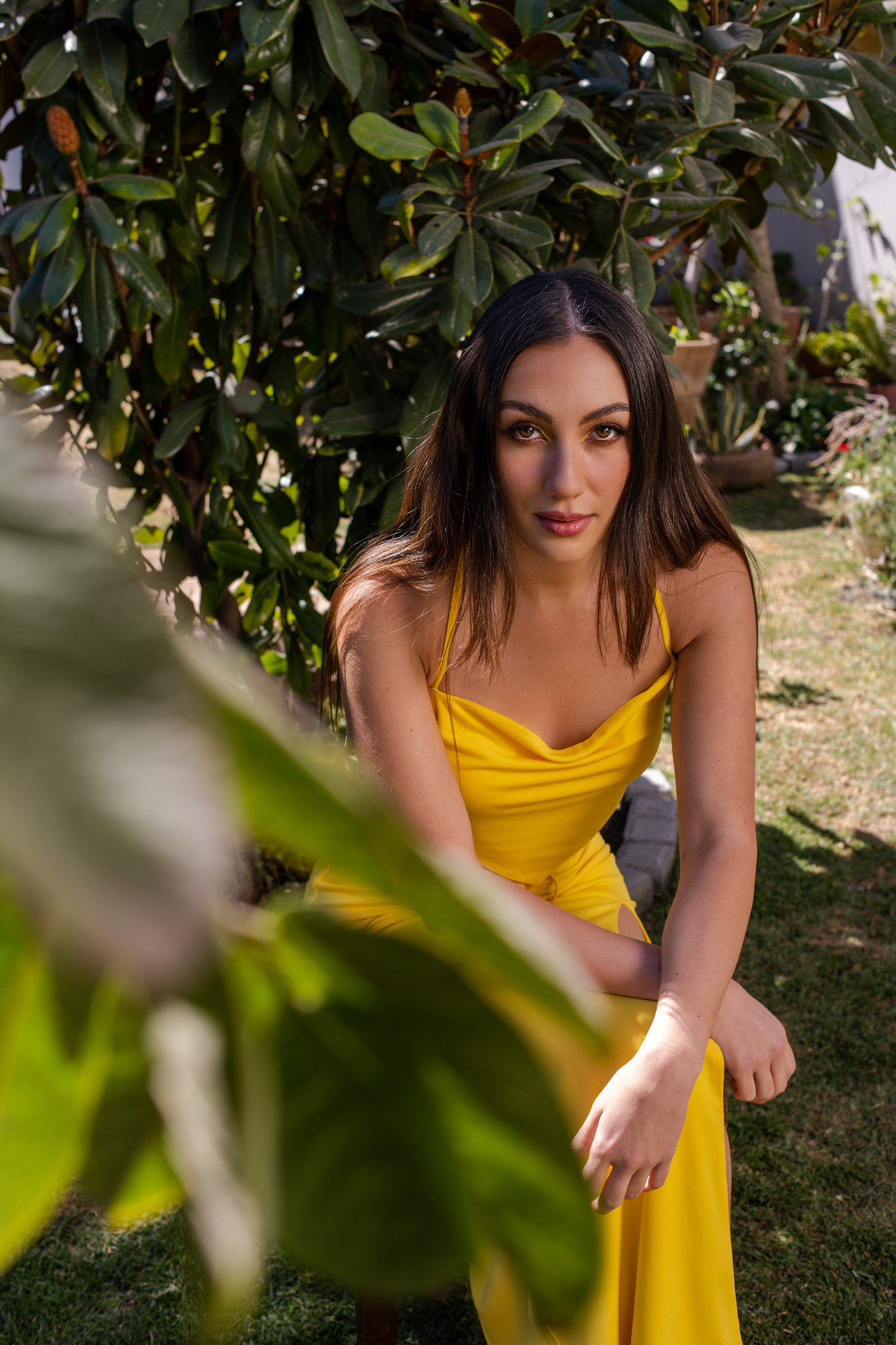 retrato editorial en exterior con modelo en vestido entallado amarillo, maquillaje profesional, a la sombra del árbol, sentada en banco de madera, puebla, méxico