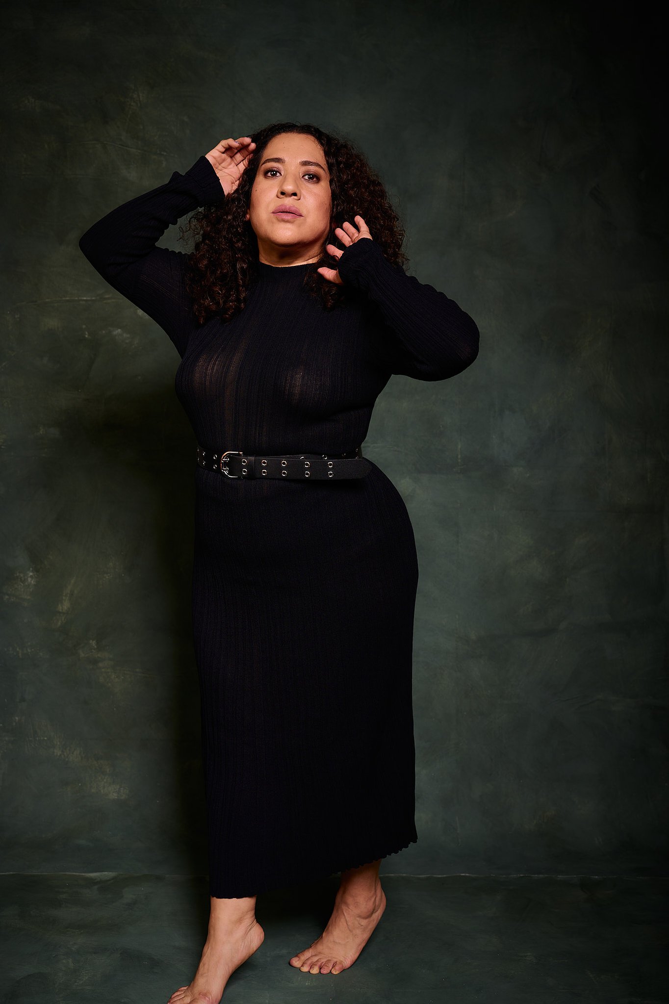 Retrato de mujer con pelo rizado y vestido transparencia negro en el estilo fotográfico de Boudoir. Fondo verde pintado a mano e iluminación de estudio.
