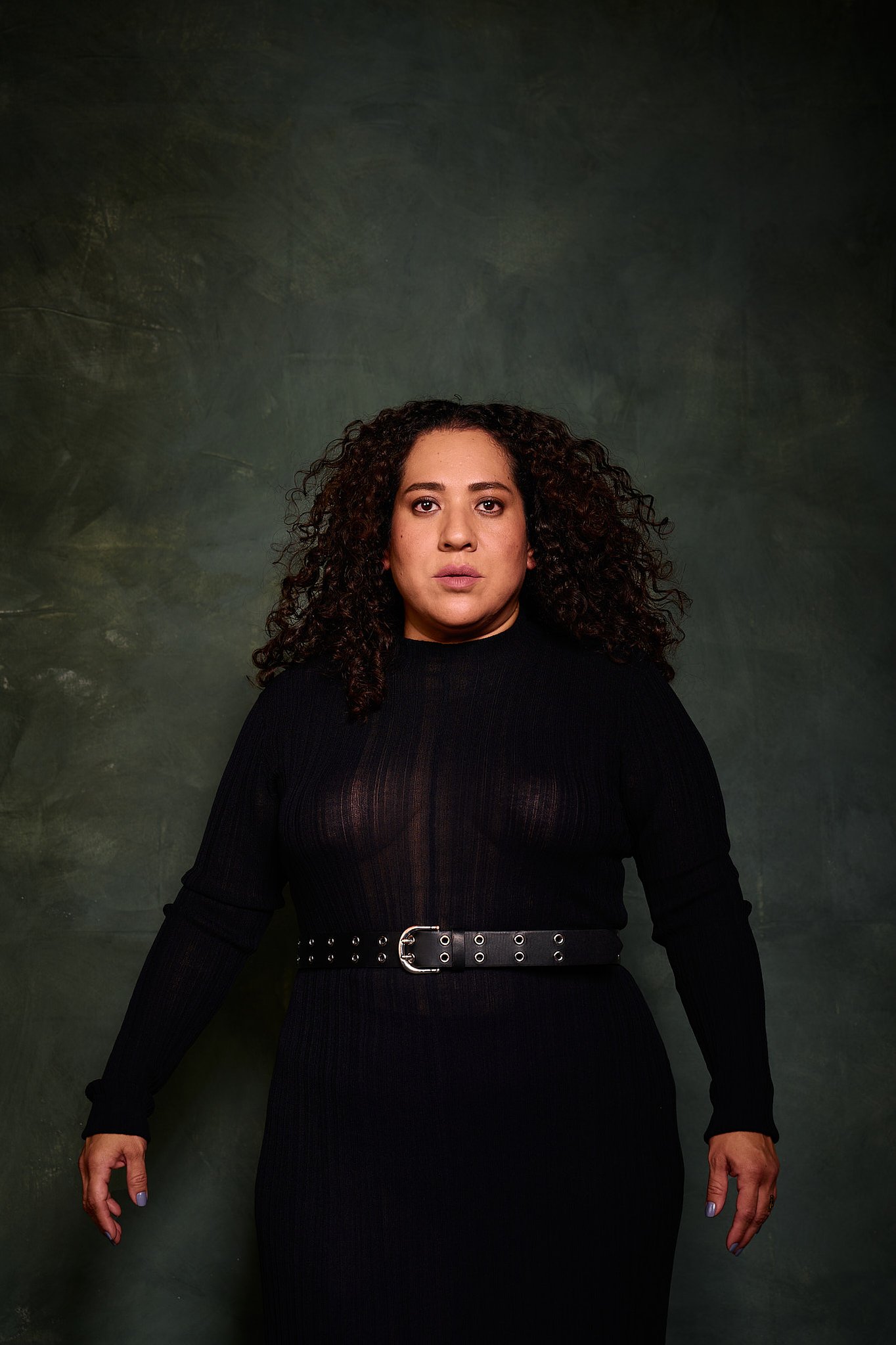 Retrato de mujer con pelo rizado y vestido transparencia negro en el estilo fotográfico de Boudoir. Fondo verde pintado a mano e iluminación de estudio.