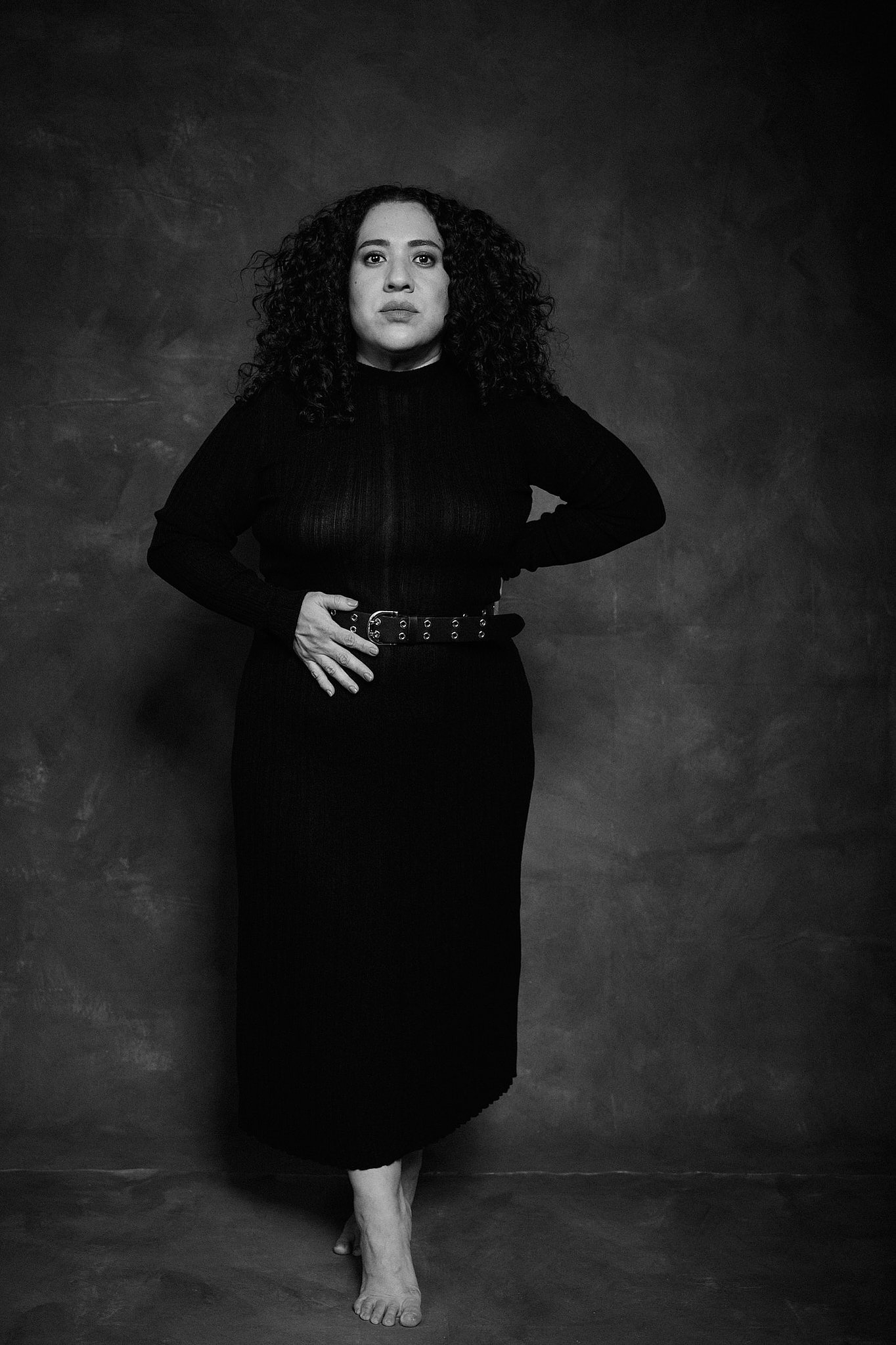 Retrato de mujer con pelo rizado y vestido de transparencia negro, en el estilo fotográfico de Boudoir. Fondo pintado a mano e iluminación de estudio.