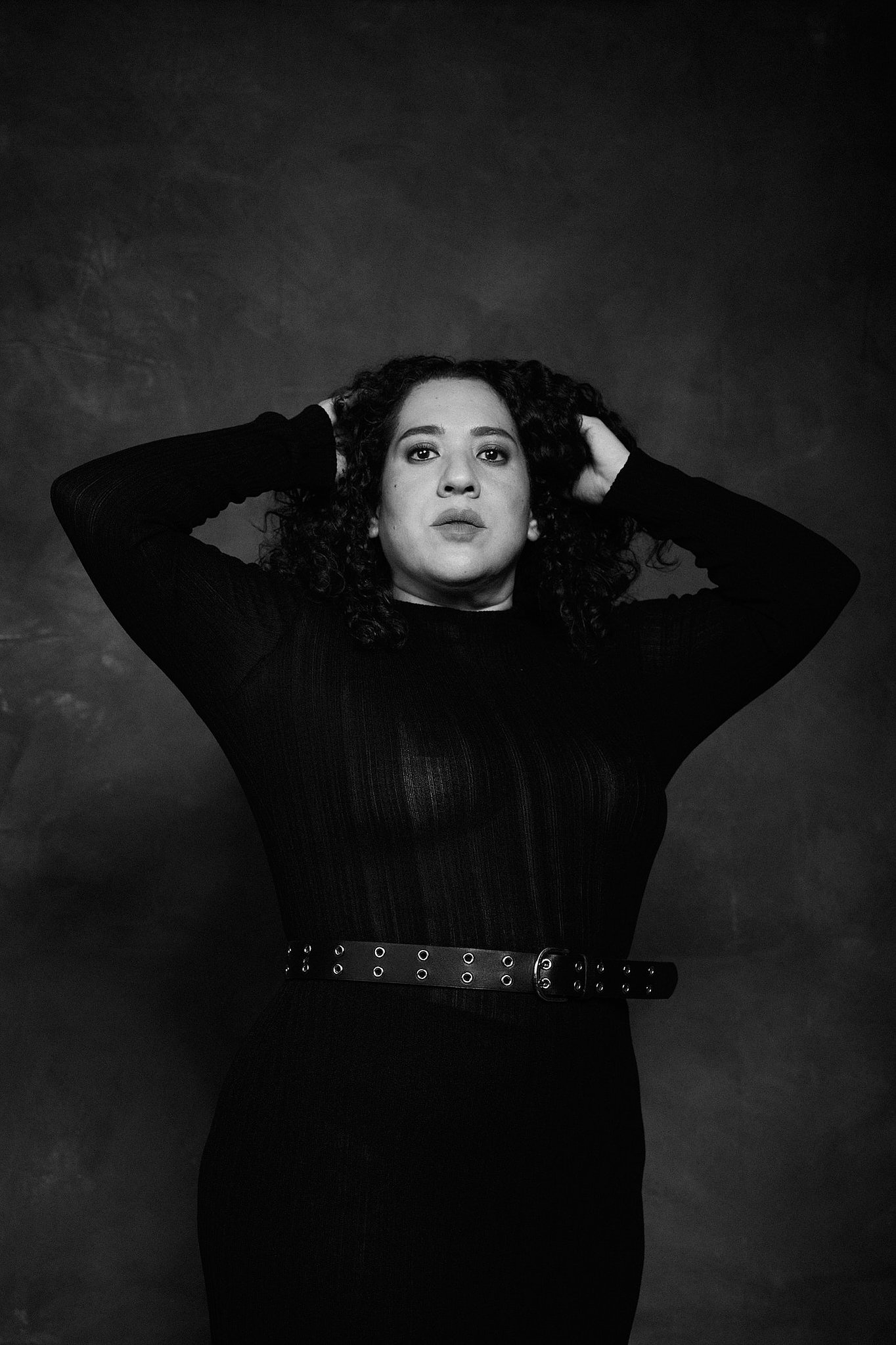 Retrato de mujer con pelo rizado y vestido de transparencia negro, en el estilo fotográfico de Boudoir.  Pose closeup de retrato dramática. Fondo pintado a mano e iluminación de estudio.
