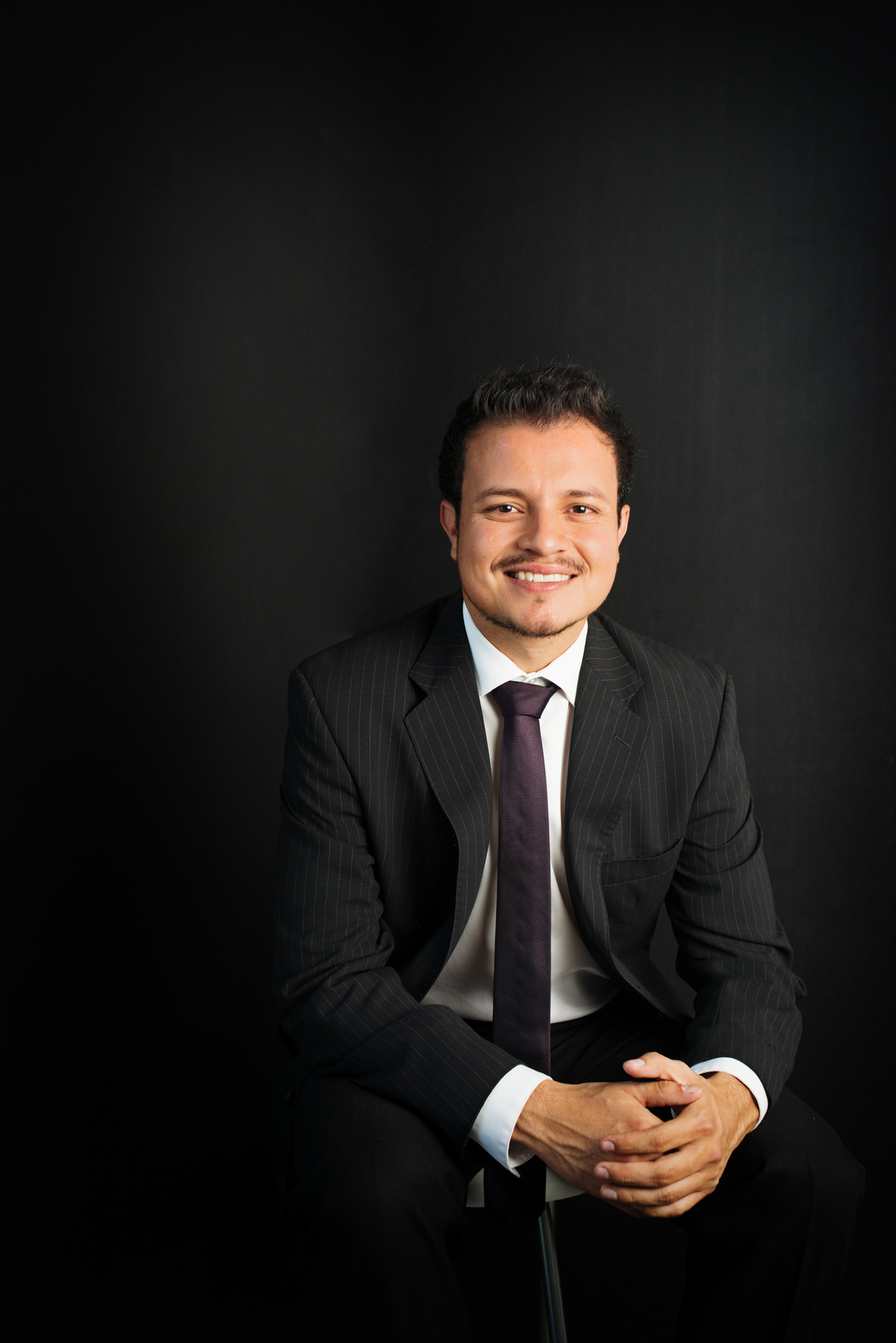 retrato corporativo headshot en estudio de hombre con atuendo profesional sentado en fondo oscuro