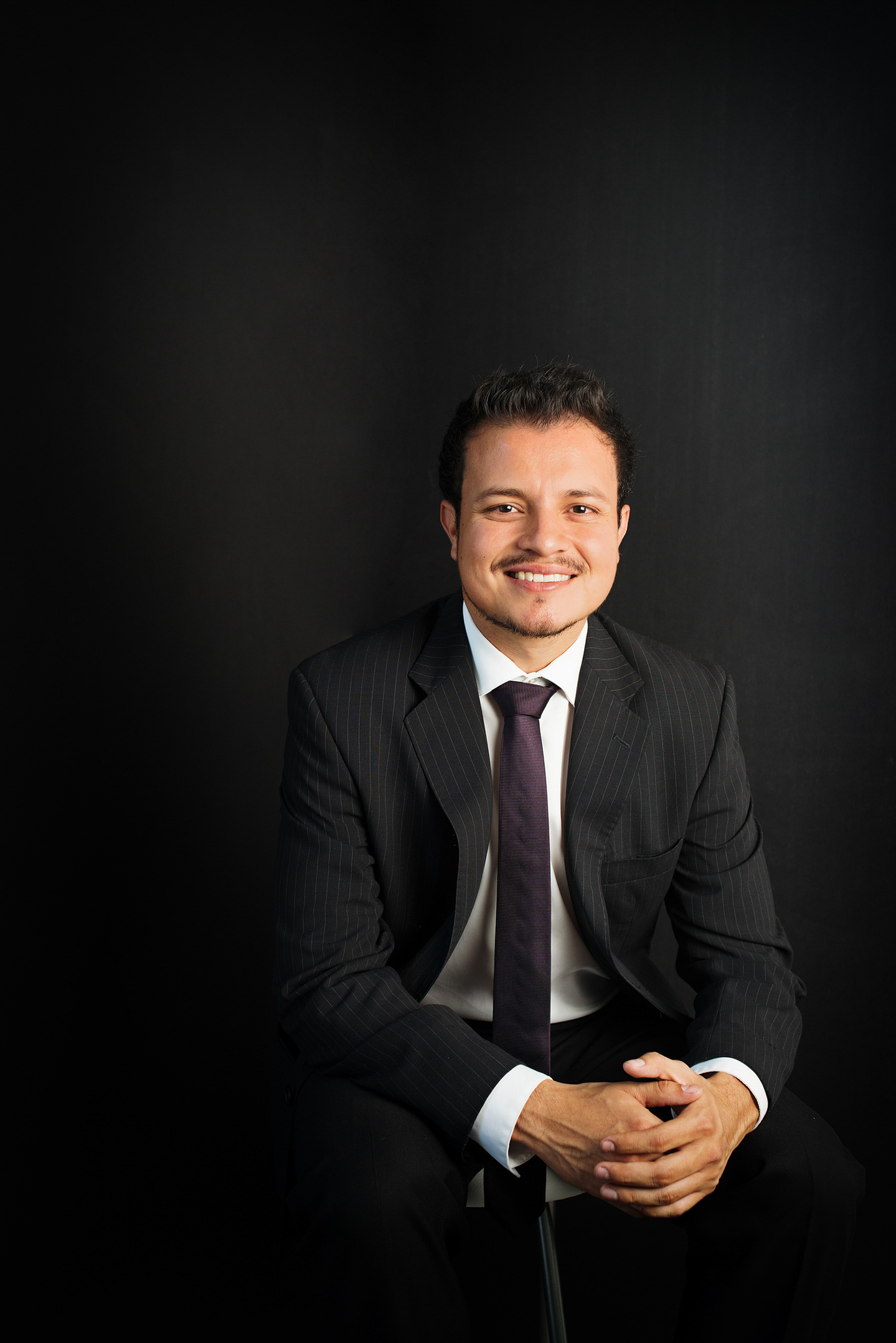 retrato corporativo headshot en estudio de hombre con atuendo profesional sentado en fondo oscuro