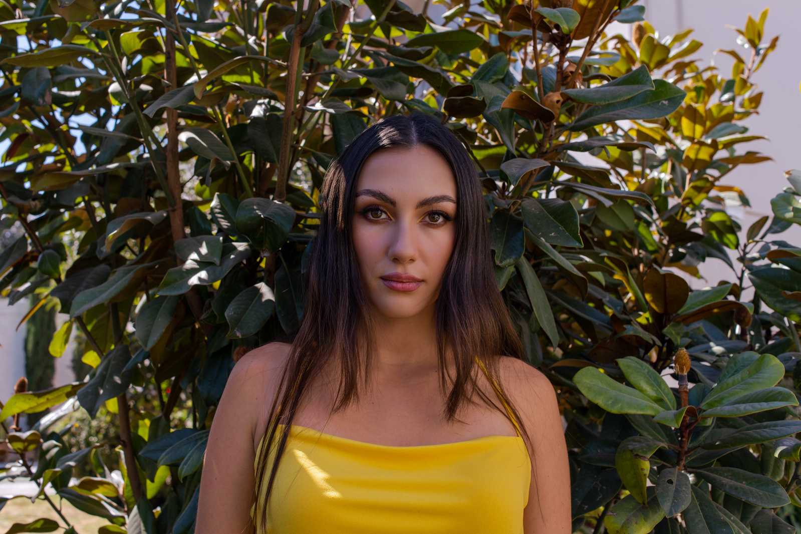 retrato editorial en exterior con modelo en vestido entallado amarillo, maquillaje profesional, a la sombra del árbol de pie viendo directo a la cámara, puebla, méxico