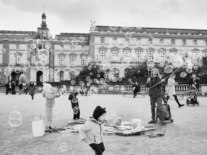A street artist at a large plaza in Paris entertains children with giant bubbles at Arc de Triomphe du Carrousel, Paris, France.
