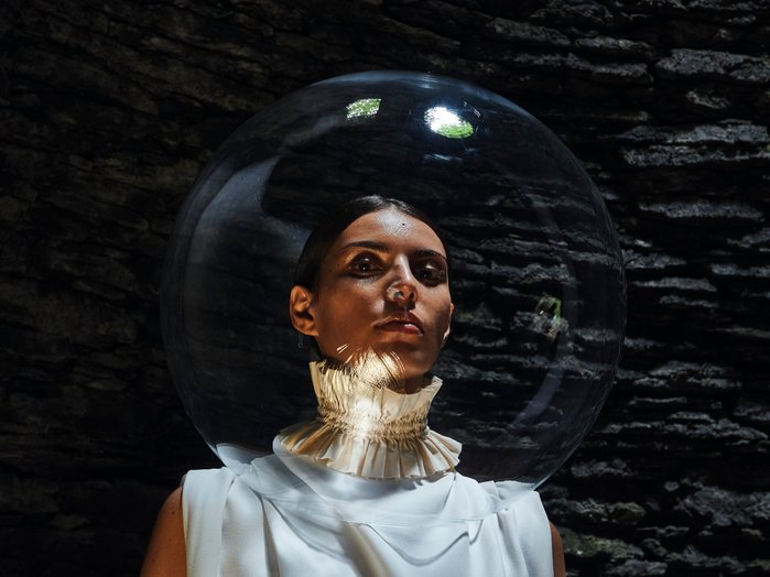 A woman stands in a cavern with a decorative collar and a glass bubble shaped helmet surrounding her head. Shot on Olympus EM1mkiii