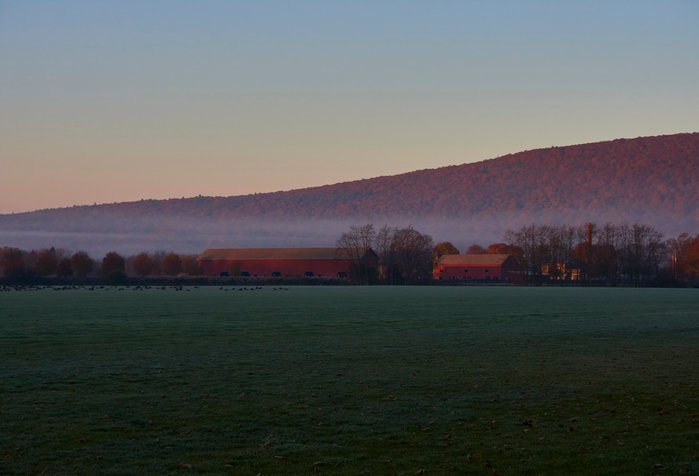 An empty polo field at dusk in the Hudson Valley with a colorful sky and gentle mist laying across the empty field. A red barn is in the background.