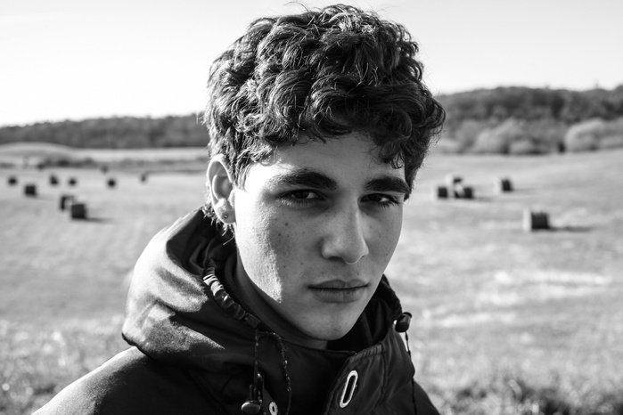 A young man standing in an open field looks straight at the camera. Shot on Canon 5dmkiv