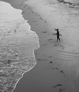 A surfer with his surfboard stands and observes the ocean before he commits his life a wave.