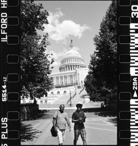 A guy with a funny hat situation walking in front of the White house. 
