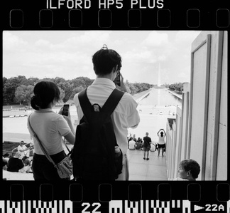 A standing international couple captures a picture of the Washington monument.