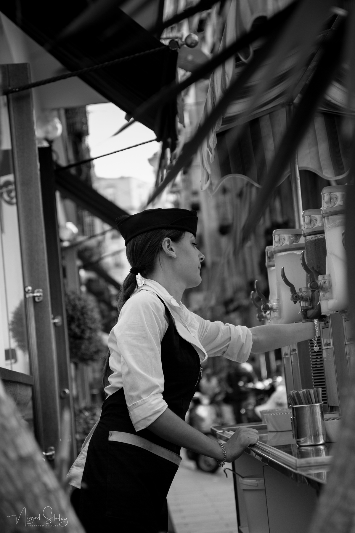 Black and white photograph shot in Naples, Italy. A stall seller selling squeezed juices to the public on a busy street corner. Nigel Sloley Photography