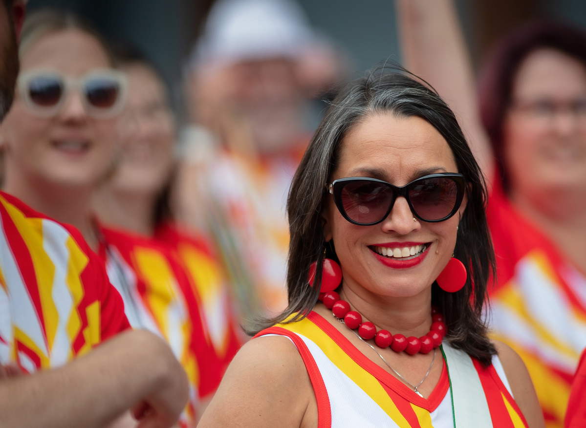 Wellington Batucada smiling female musician, wearing red, white, and yellow costume and dark glasses shot by Nigel Sloley Photography at New Zealand's Cuba Dupa Street carnival in Wellington.