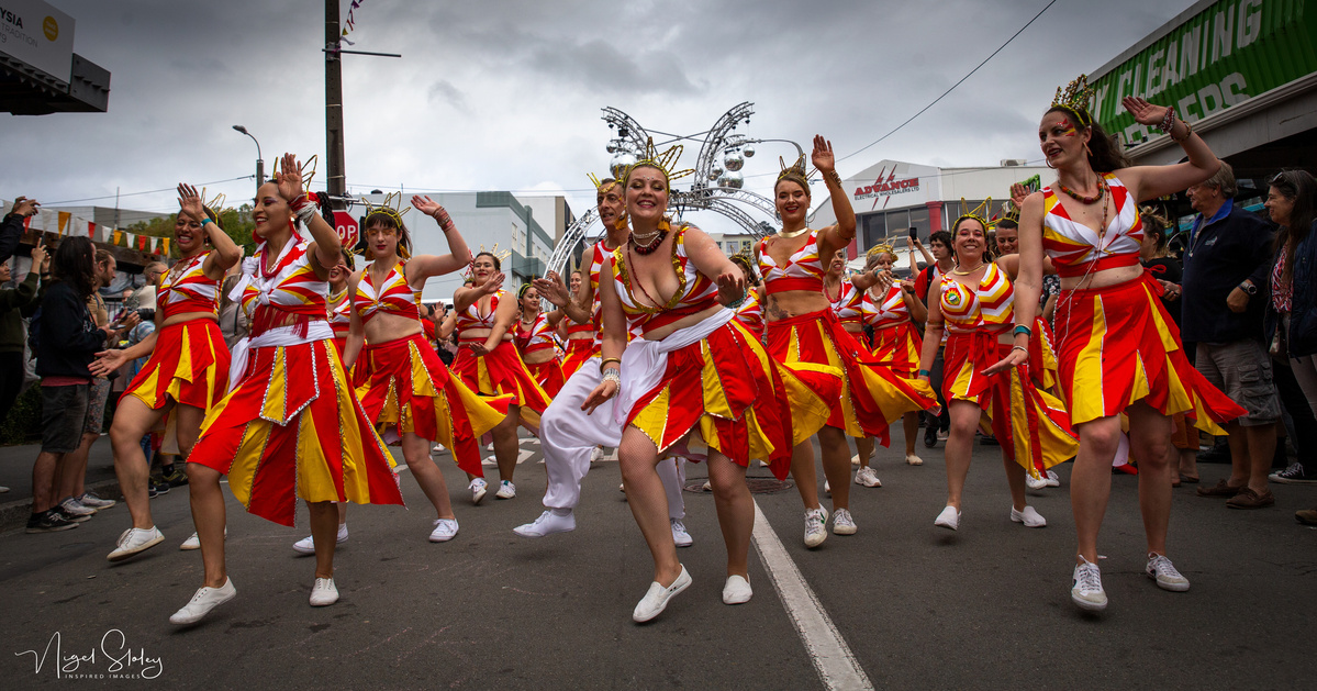 Wellington Batucada dancers wearing red and yellow costumes dancing and parading in the street shot by Nigel Sloley Photography at New Zealand's Cuba Dupa Street carnival in Wellington.