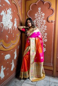 Portrait photoshoot of a model wearing a pink gold and orange coloured saree resting against a wall with white tribal paintings professionally shot by best advertising photographer in Mumbai India.
