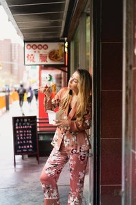 Russian model leaning against wall wearing pink floral designer clothing eating chinese food based in Manhattan New York shot by award winning fashion photographer from Mumbai Santacruz India