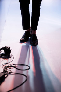a professional photograph of a male model's legs with black headphones and wires scattered in front of him with his shadow on a white floor shot by best advertising photographer ashish gurbani based in pune india 